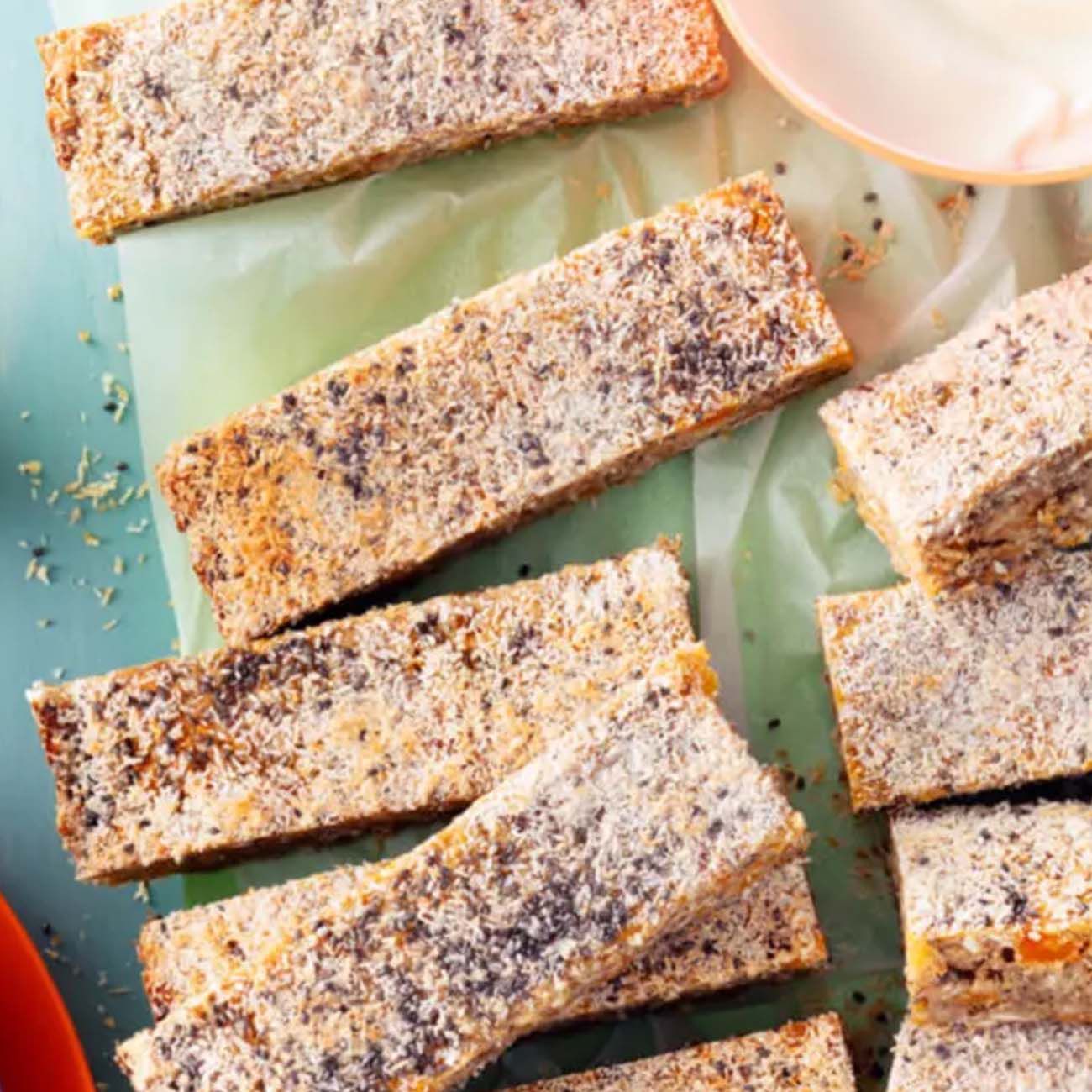 Homemade muesli bars coated in desiccated coconut, sliced and arranged on light green greaseproof paper.