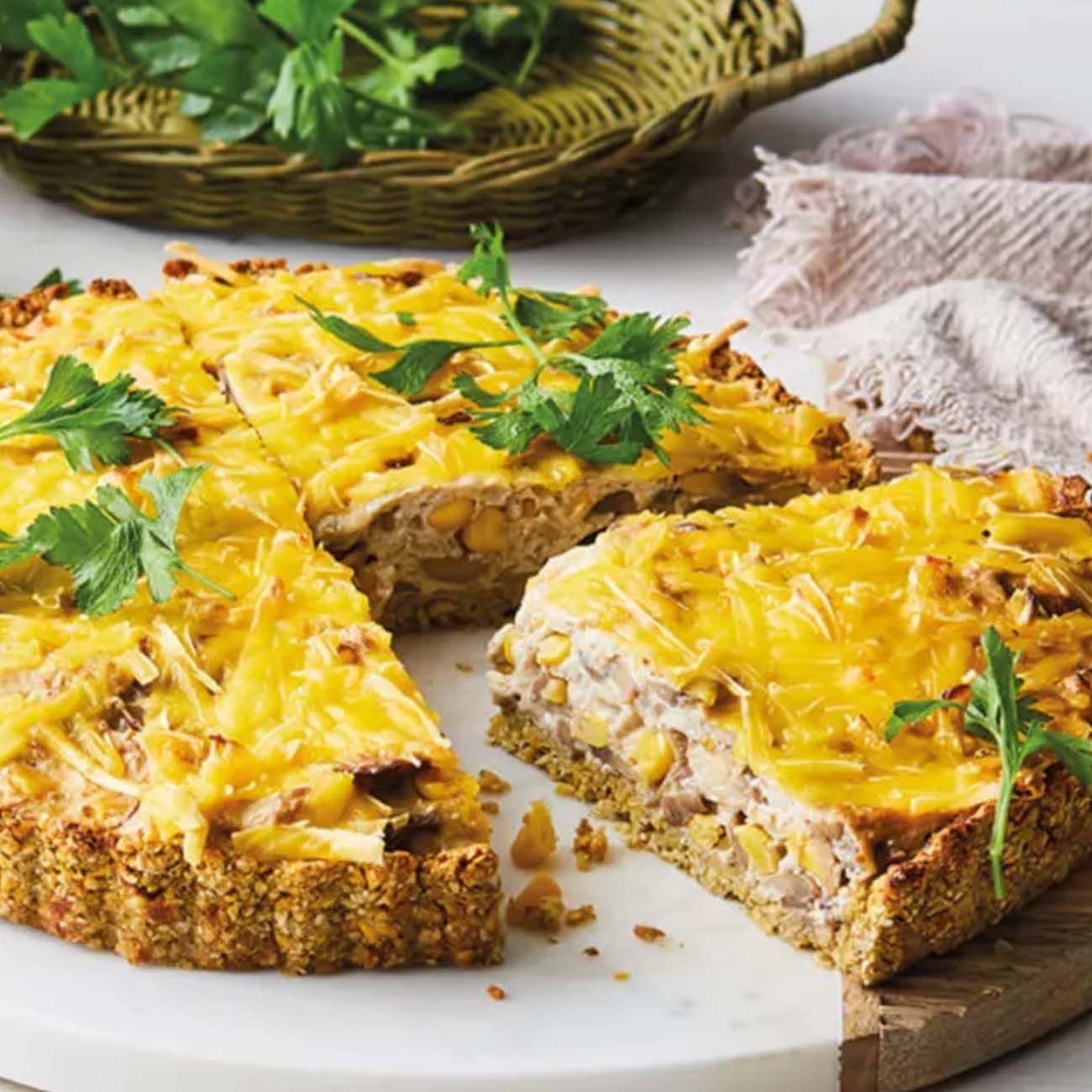 A savoury tart or quiche with a golden oat crust, filled with corn and vegetables and topped with melted cheese and parsley.