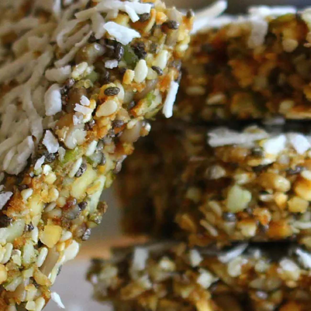 Close-up of a stacked seed slice packed with sesame seeds, chia seeds and grains, topped with shredded coconut.