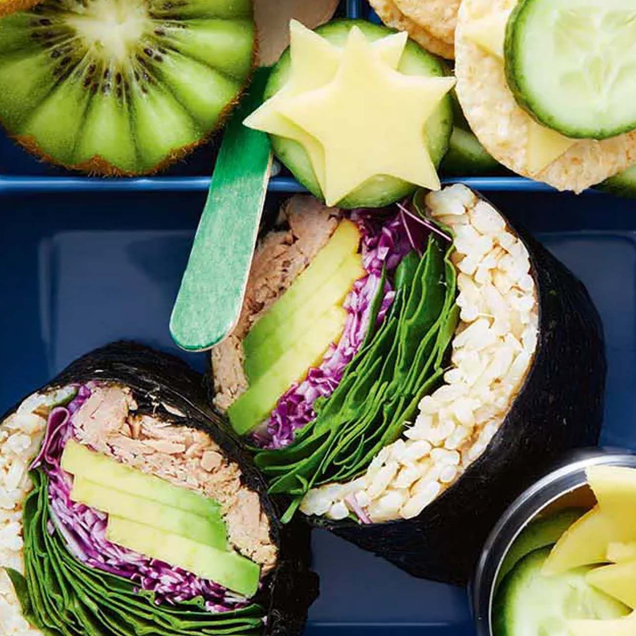 A blue lunch box filled with a tuna and avocado sushi sandwich, half a kiwi fruit, cucumber slices and cheese stars.