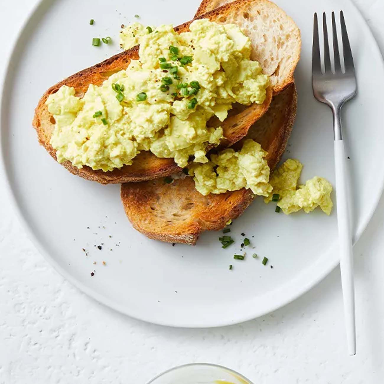 Creamy scrambled eggs on slices of toasted sourdough bread, garnished with chopped chives on a white plate.