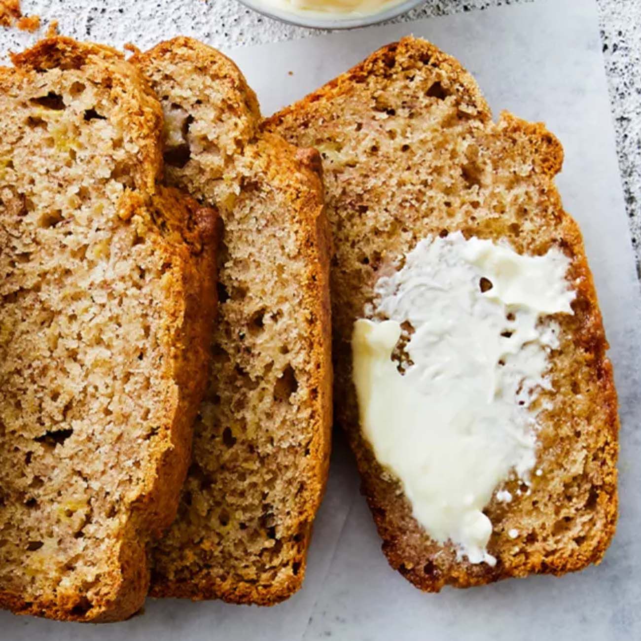 Three thick slices of toasted banana bread, with the top slice generously spread with melting butter.