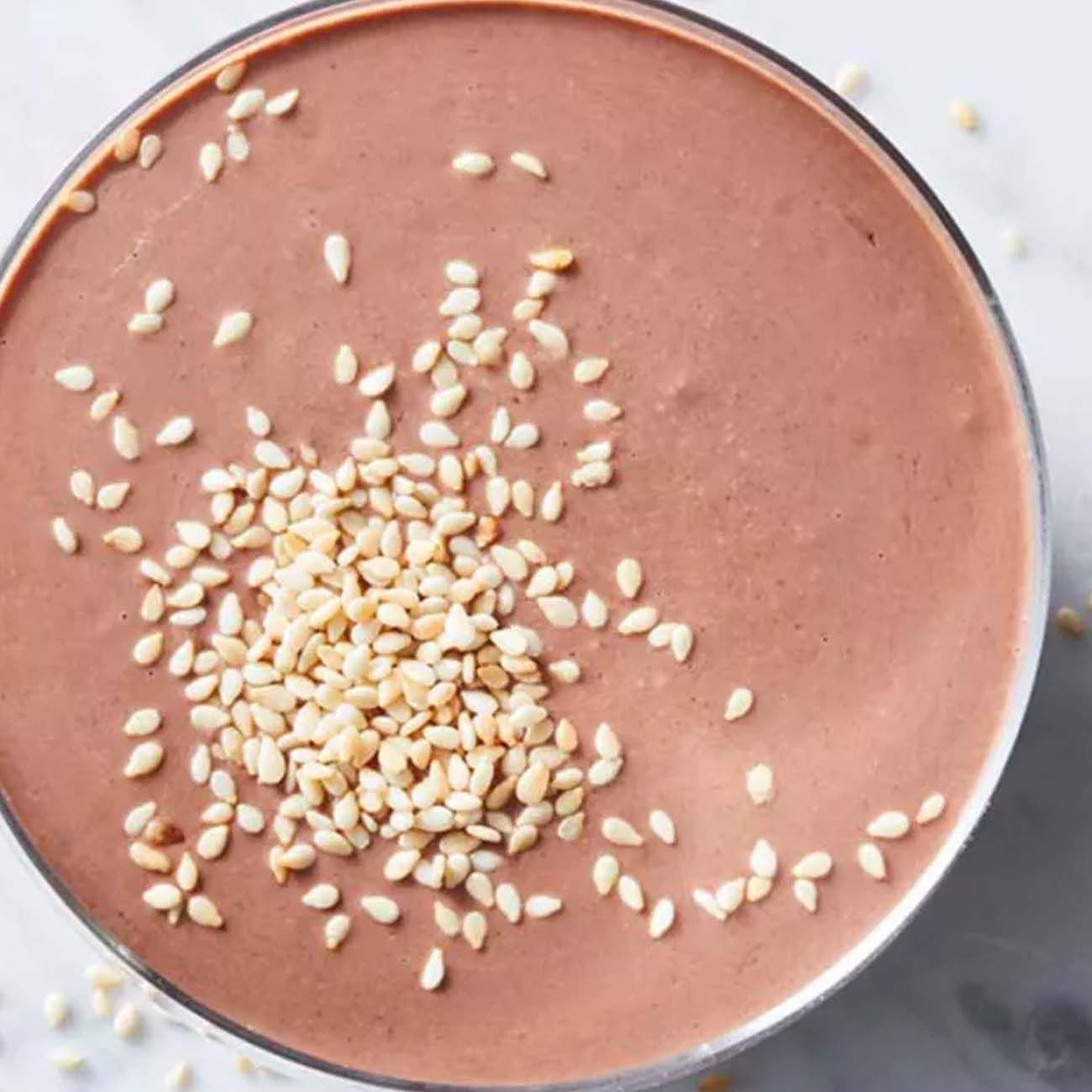 An overhead view of a smooth chocolate smoothie or dip in a glass, garnished with a sprinkle of sesame seeds.