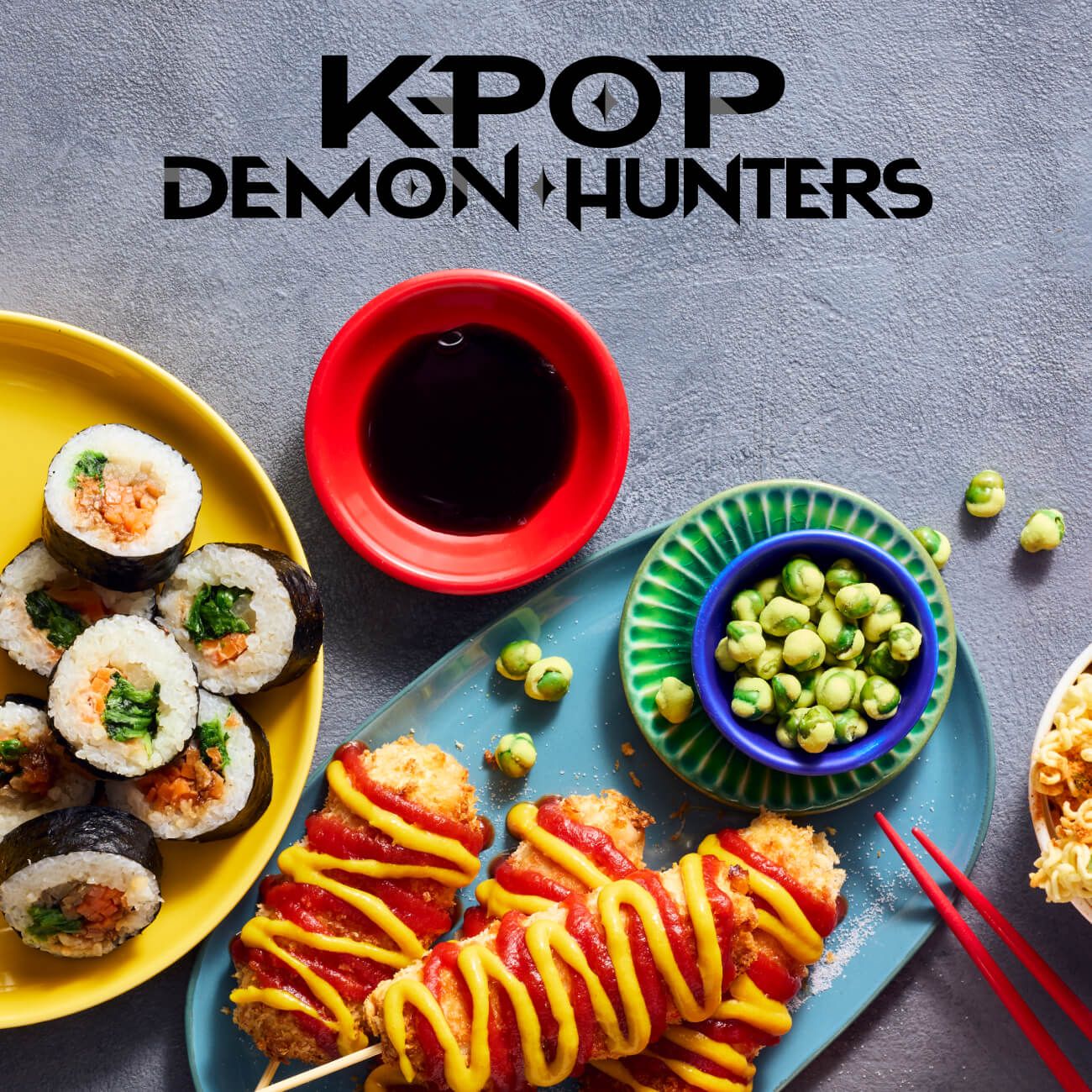 Overhead view of sushi, corn dogs, and snacks with the "KPOP DEMON HUNTERS" logo.