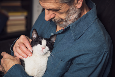 A man with a beard hugging a sleeping black and white cat against his chest.