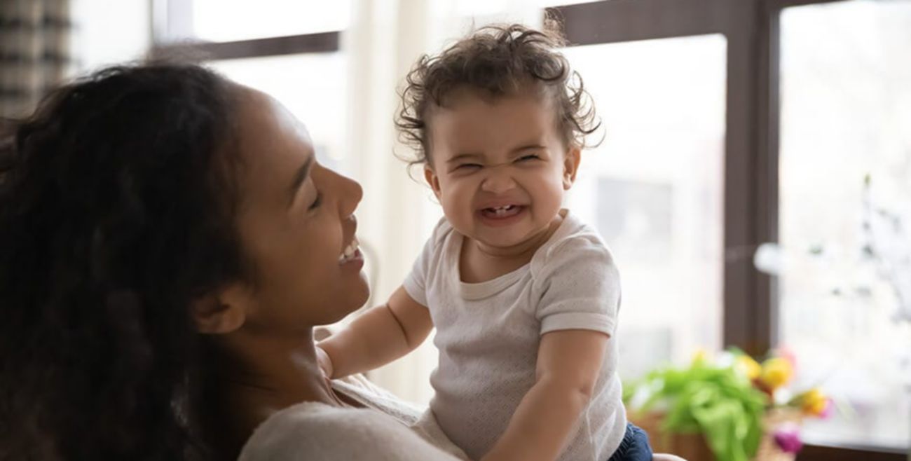 Happy mother holding a smiling baby revealing four tiny front teeth.