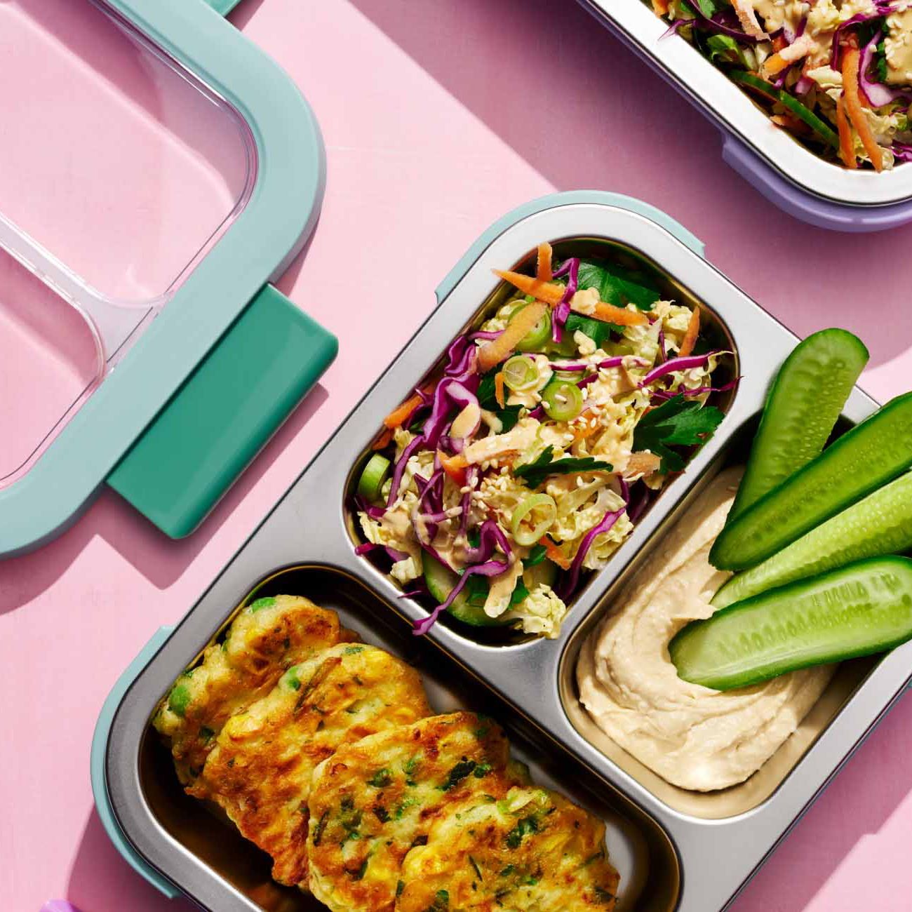 Close-up of a stainless steel bento lunch box packed with cabbage salad, sliced cucumber, and dip