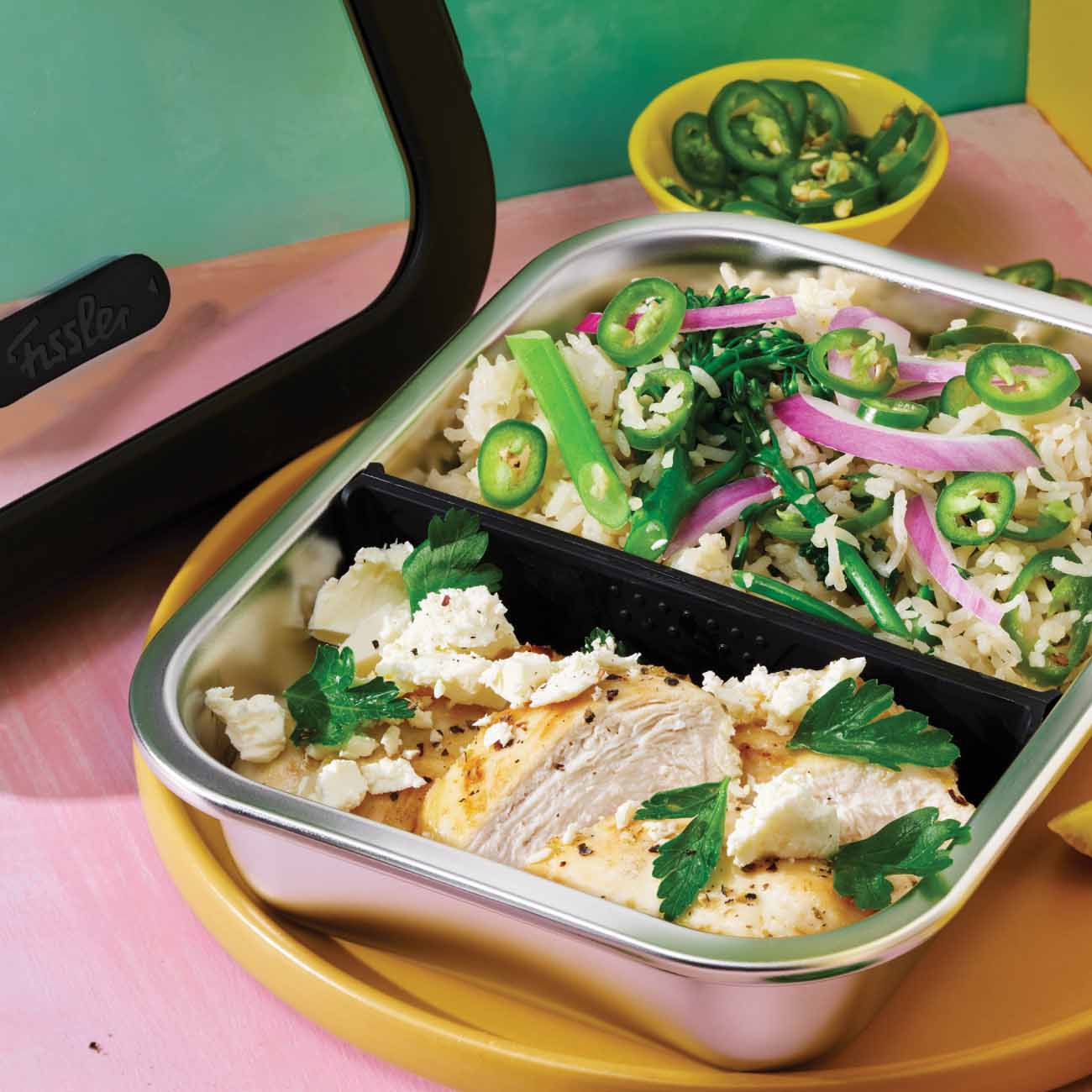 Stainless steel bento box packed with sliced chicken breast, rice salad, and green chillies