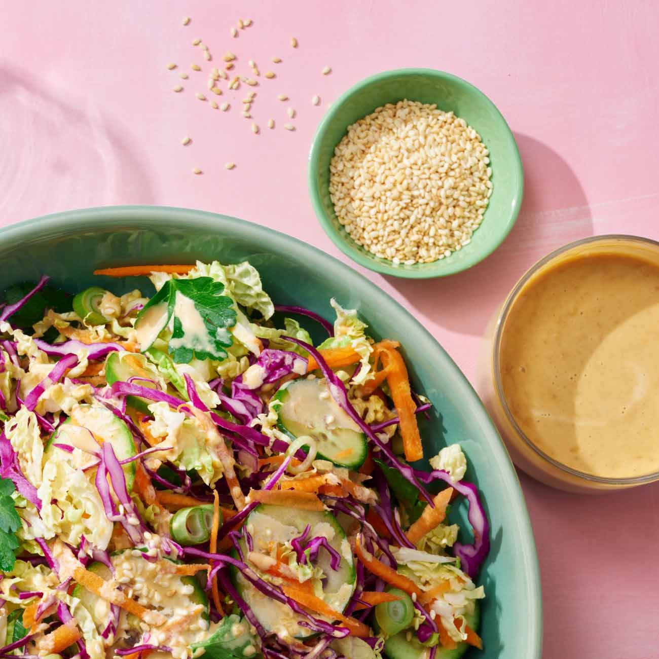 Overhead view of a large salad bowl with shredded cabbage and carrots next to sesame seeds and dressing
