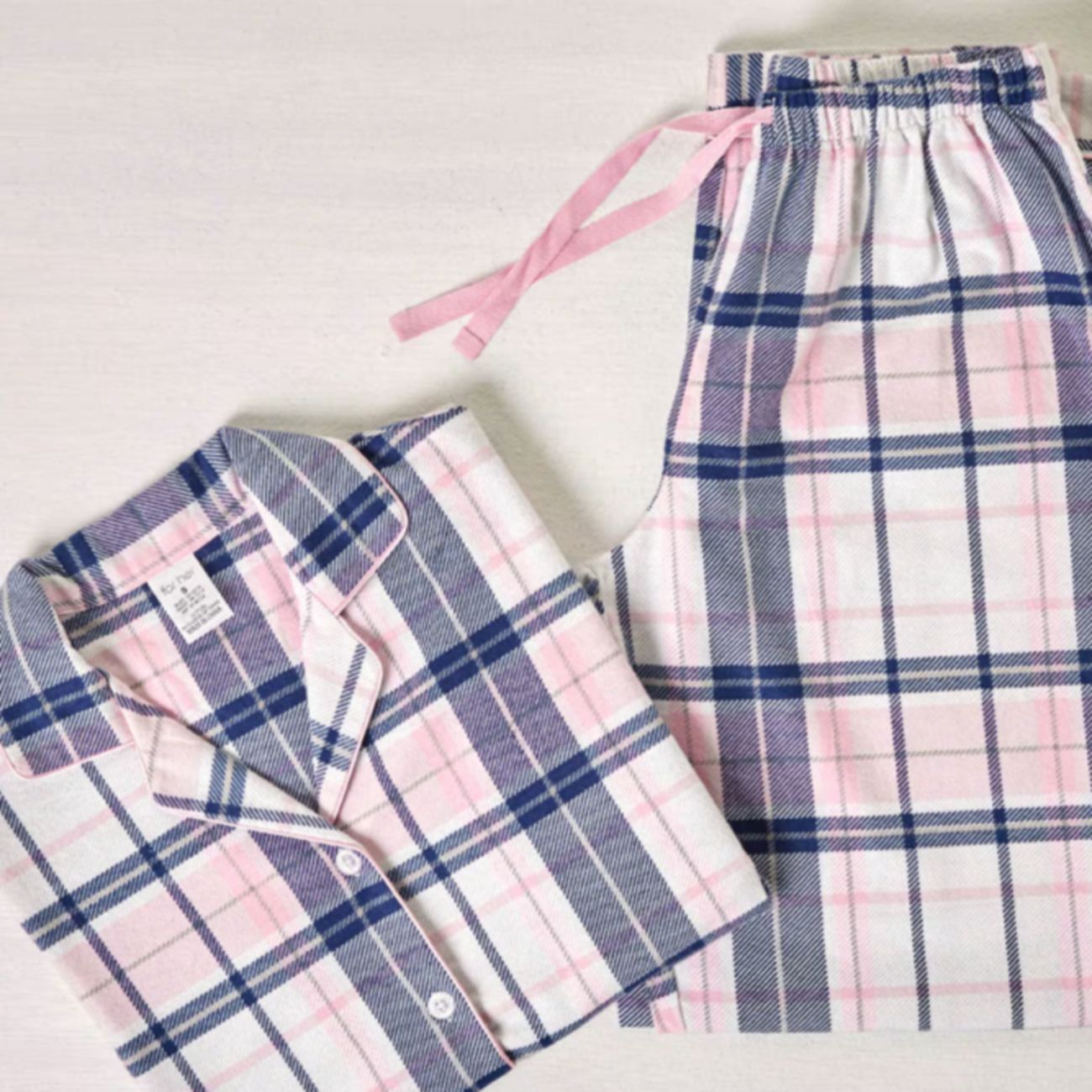Folded pink, navy, and white checked pyjama shirt and matching drawstring pants on a white surface.