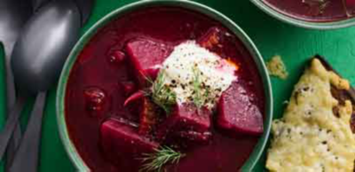 A vibrant, deep red beetroot soup served in a green bowl, topped with sour cream, dill and fresh black pepper.