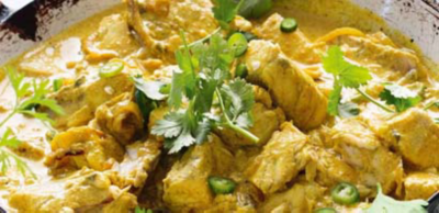 A creamy, yellow fish curry cooking in a pan, garnished with sliced green chillies and fresh coriander sprigs.
