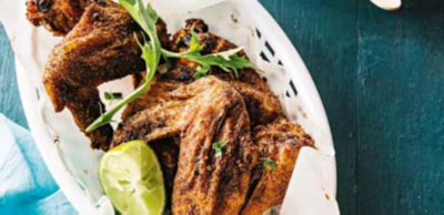 Crispy, spice-rubbed chicken wings served in a white basket lined with paper, garnished with a lime wedge and leafy greens.