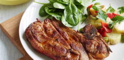 A seared lamb chop served on a white plate with baby spinach leaves and a potato salad with capsicum and parsley.