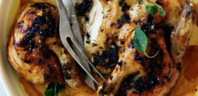 A roasted spatchcock chicken with crispy, herb-rubbed skin, served in juices and garnished with fresh oregano leaves.
