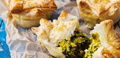 Golden puff pastry pies on baking paper, with one pulled apart to reveal a green spinach and yellow egg filling.