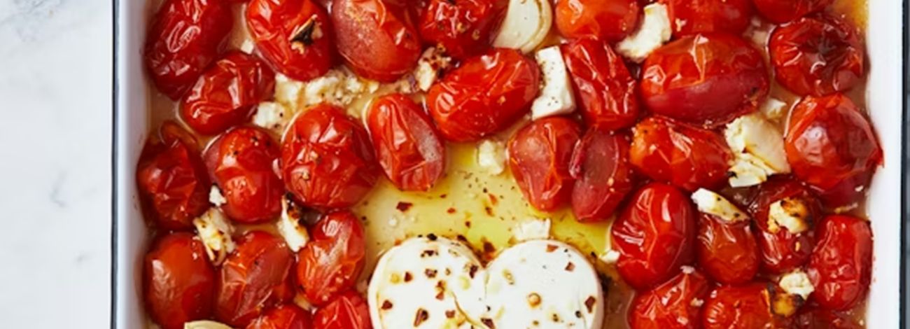 Roasted cherry tomatoes and garlic surrounding a heart-shaped block of feta cheese seasoned with chilli flakes.