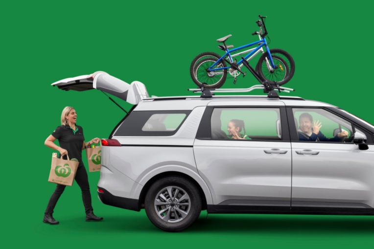 Woolworths person putting grocery bags in boot of wagon with bikes on the roof rack.